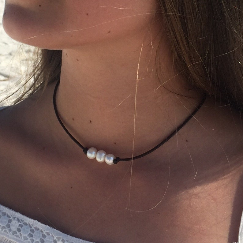May include: A simple black leather choker necklace with three white pearls.