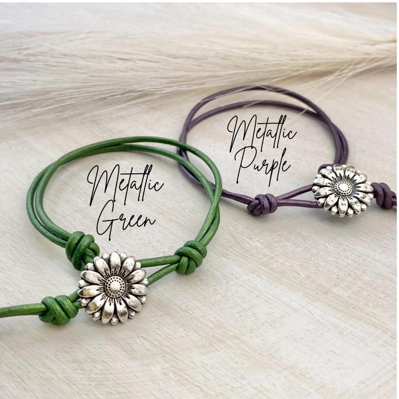 May include: Two adjustable bracelets, one metallic green and one metallic purple, each featuring a daisy-shaped charm. The bracelets are displayed on a light-colored surface, with the words "Metallic Green" and "Metallic Purple" written on them.