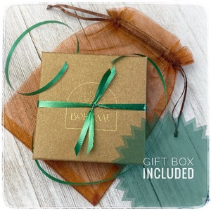May include: A brown gift box with a green ribbon tied around it. The box has a gold logo that says "BOH&Egrave;ME". The box is sitting on a brown and white patterned fabric. The text "GIFT BOX INCLUDED" is printed in white on a green background.