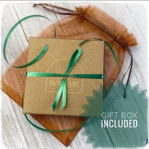 May include: A square, brown gift box tied with a green ribbon, with the word "BOHEME" printed on the front. The box is on top of a sheer, brown drawstring bag. The words "GIFT BOX INCLUDED" are printed on a green background.