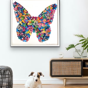 May include: A framed artwork featuring a colorful butterfly made of smaller butterflies. The butterfly is a collage of various colors and patterns, including blue, green, yellow, orange, and pink. The artwork is displayed on a white wall in a modern living room setting.