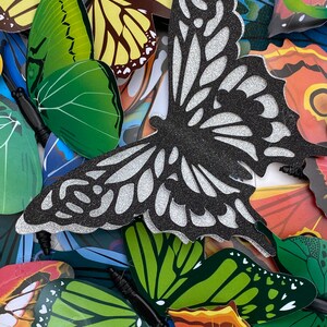 May include: A collection of colorful butterfly decorations with glitter accents. The butterflies are made of paper and have a variety of patterns and designs.