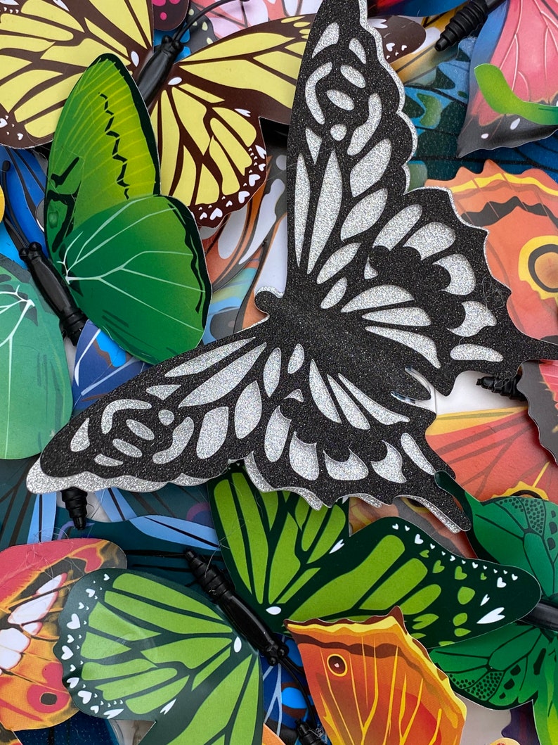 May include: A collection of colorful butterfly decorations with glitter accents. The butterflies are made of paper and have a variety of patterns and designs.