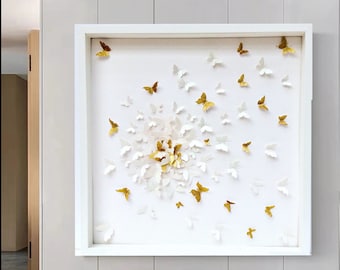 May include: A white framed wall art piece featuring a white paper flower with gold glitter butterflies surrounding it.