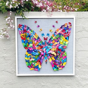 May include: A framed artwork featuring a large butterfly made of colorful butterflies. The butterfly is surrounded by a white frame and a gray background.