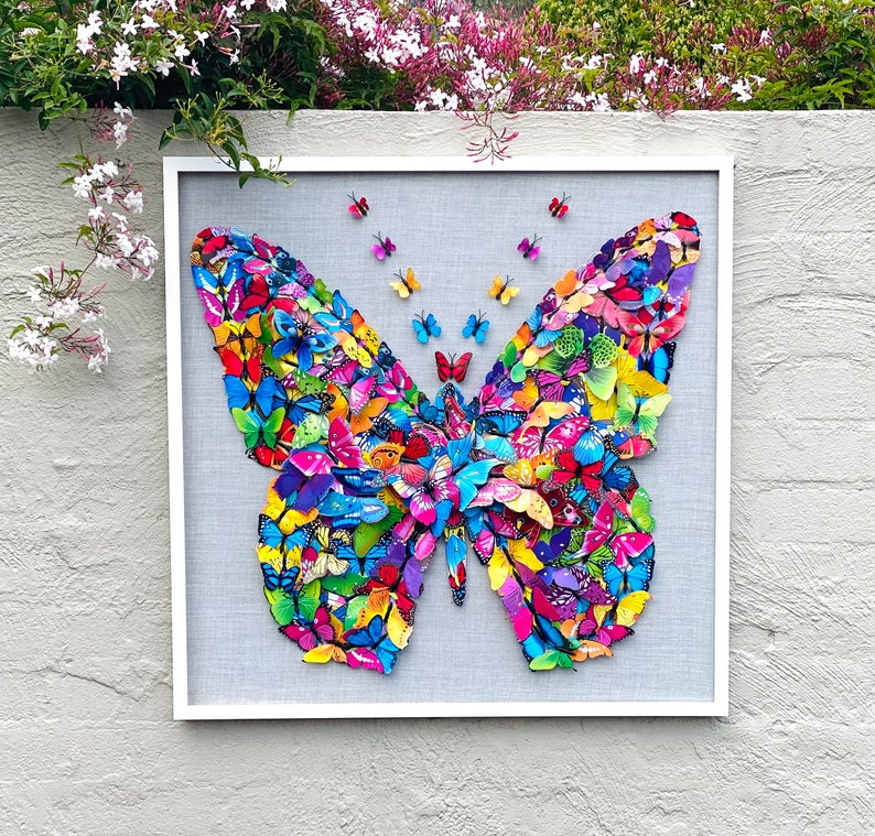 May include: A framed artwork featuring a large butterfly made of colorful butterflies. The butterfly is surrounded by a white frame and a gray background.