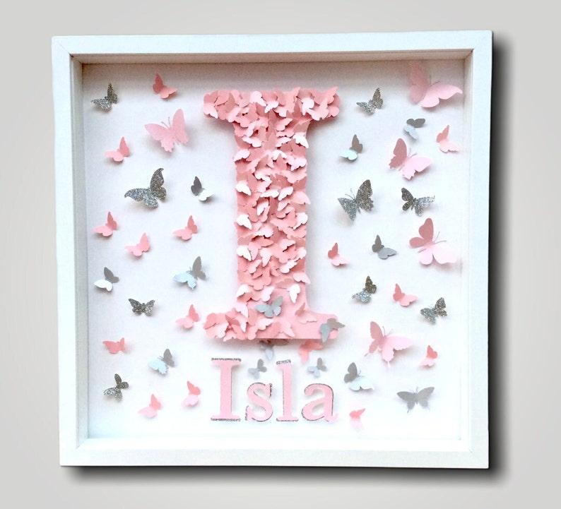 May include: A white frame with a pink letter I made of pink butterflies. The name Isla is written below the letter. There are silver glitter butterflies scattered around the letter and name.