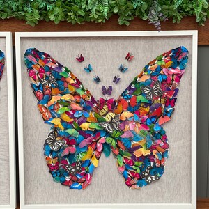 May include: A framed wall art piece featuring a large butterfly made of many smaller butterflies in various colors, including blue, green, red, yellow, and purple.