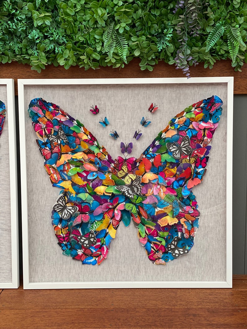 May include: A framed wall art piece featuring a large butterfly made of many smaller butterflies in various colors, including blue, green, red, yellow, and purple.