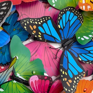 May include: A collection of colorful butterfly decorations with various patterns and designs. The butterflies are made of paper or plastic and have a 3D effect. They are perfect for adding a touch of whimsy to any space.