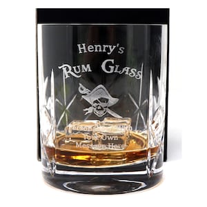 May include: A personalized glass etched with "Henry's Rum Glass" and a pirate skull and crossbones design. The glass is filled with amber liquid and ice cubes.