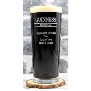 Op de afbeelding: Een hoog, helder glazen pintglas met een zwarte vloeistof erin. Het glas is gegraveerd met de woorden "GUINNESS ORIGINAL" en een gepersonaliseerd bericht: "Happy 21st Birthday Son Lots of love Mum & Dad xx".