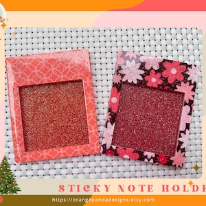 May include: Two rectangular sticky note holders. One is red with a white floral pattern, the other is red with a floral design. Both have a glittery red interior. The text "STICKY NOTE HOLDER" is at the bottom.