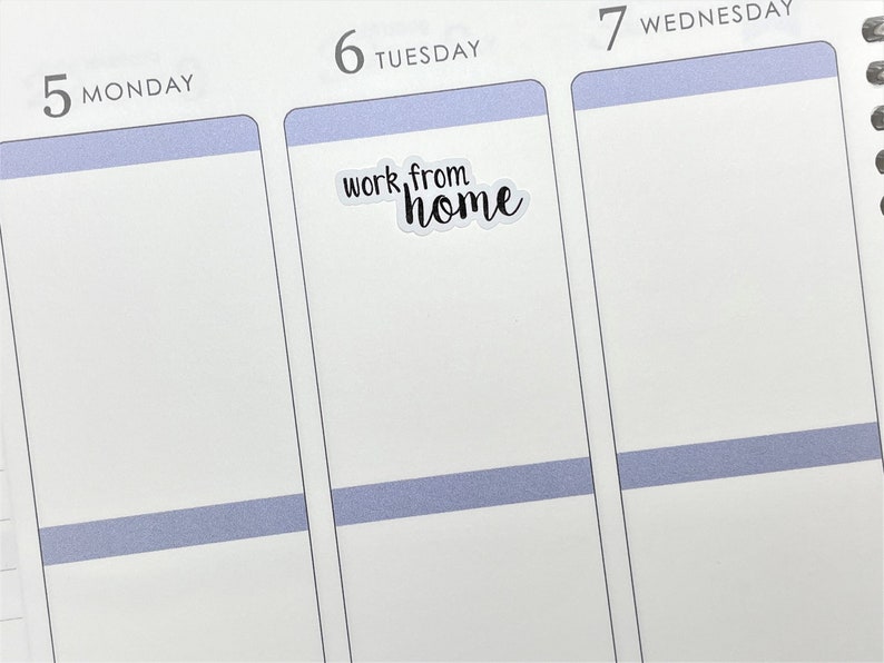 May include: A white planner with a blue stripe across the top of each day. The day "Tuesday" is highlighted with a sticker that says "work from home" in black cursive writing.