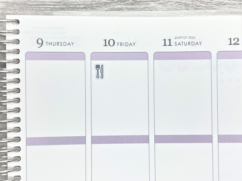 May include: A close-up of a weekly planner with a sticker of a fork and knife on the Friday page. The planner has a light purple stripe across the top of each day.