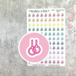 Può includere: Un foglio di adesivi a tema ginnastica con una varietà di disegni di anelli colorati. Un grande adesivo rosa con un disegno ad anello è in primo piano. Tre adesivi rosa a forma di cuore sono a destra. Il testo "NooNoo & Bob" e "405 - Gymnastics Icon" sono visibili.