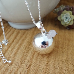 Peut inclure: Un collier en argent avec un grand pendentif rond en argent. Le pendentif est orné d'une petite pierre précieuse rose. Le collier est sur un fond en tissu jaune.