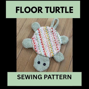 May include: A handmade floor turtle sewing pattern. The turtle has a colorful shell with pink, orange, and white stripes. The head and limbs are a soft green color, and the eyes are black. The text "FLOOR TURTLE" and "SEWING PATTERN" are displayed.