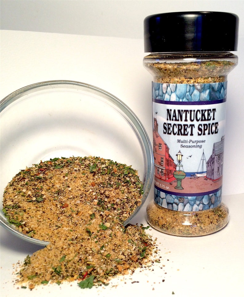 Pu&ograve; includere: Un barattolo di vetro di condimento multiuso Nantucket Secret Spice. Il barattolo &egrave; pieno di una miscela di erbe e spezie. L'etichetta presenta una scena di mare con un faro e una barca a vela.