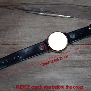Pu&ograve; includere: Cinturino da orologio in pelle nera con quadrante bianco. Il cinturino &egrave; lungo 21 cm. "SI PREGA di controllare la dimensione prima di ordinare" &egrave; scritto sulla superficie in legno.