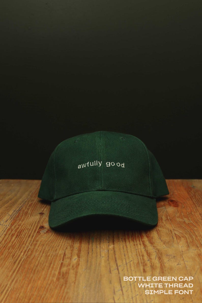 May include: A bottle green baseball cap featuring the text "awfully good" embroidered in white thread across the front. The cap has a structured crown and a curved brim, with the text "BOTTLE GREEN CAP WHITE THREAD SIMPLE FONT" visible.