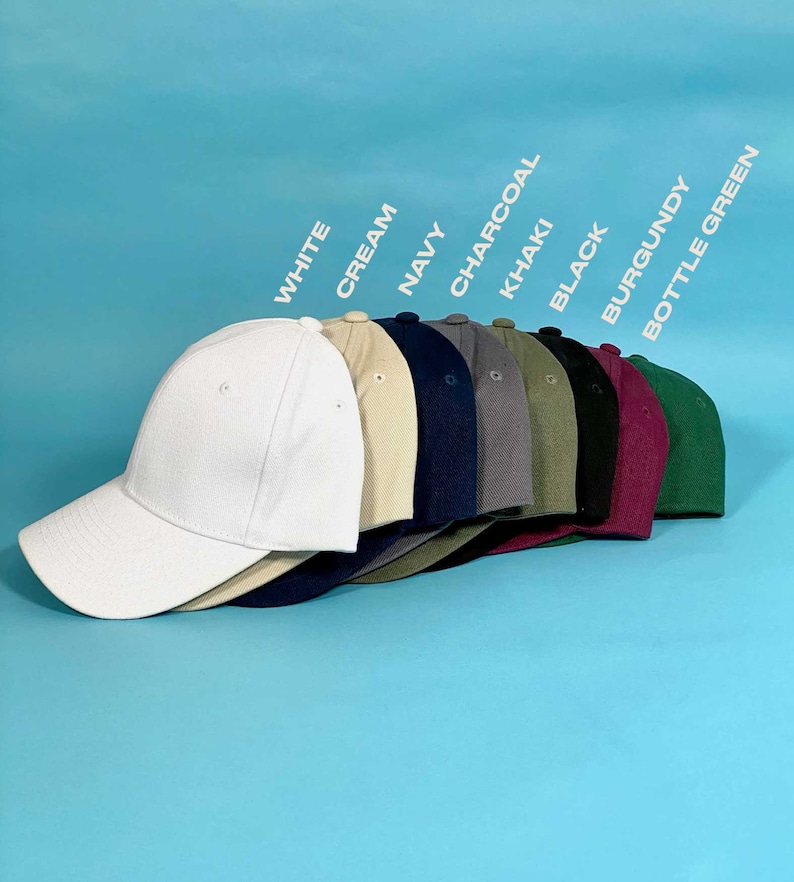 May include: A row of eight baseball caps in various colors including white, cream, navy, charcoal, khaki, black, burgundy, and bottle green. Each cap features a structured crown, a curved brim, and a button on top, arranged in a cascading line.