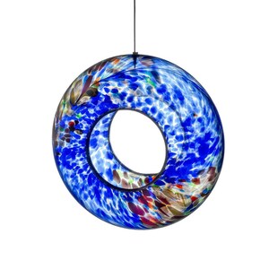 May include: A circular, hollow glass ornament featuring a vibrant blue speckled pattern with accents of white, red, and brown. The piece is suspended by a thin black cord, showcasing a smooth, polished surface and a central open void.