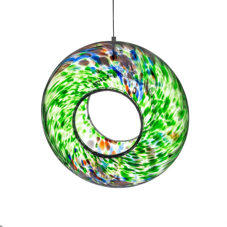 May include: A circular glass bird feeder featuring a vibrant speckled pattern of green, blue, and orange hues. The hollow center provides an opening for birds, and the piece is suspended by a thin black cord attached to the top rim of the glass.