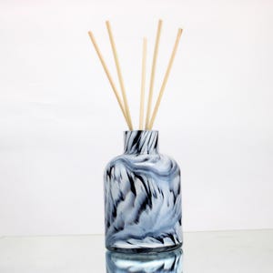 May include: A decorative glass diffuser bottle with a marbled blue and black pattern. The bottle contains several light-coloured wooden reeds. The product is designed for home fragrance and aromatherapy.
