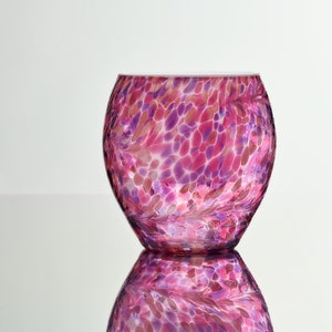 May include: A pink and purple glass vase with a speckled pattern. The vase is round and has a wide opening.
