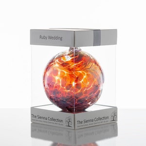 May include: A ruby red glass bauble in a clear box with the text "Ruby Wedding" and "The Sienna Collection Inspirational Hand Crafted Art Glass" on the box.