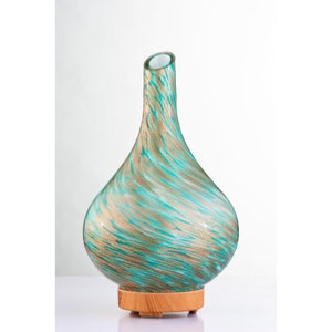 May include: A teal and gold swirl glass essential oil diffuser with a wooden base.