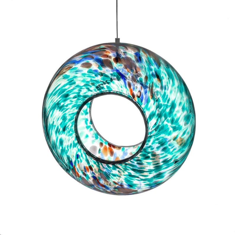 May include: A circular, hollow glass pendant light featuring a swirling, mottled pattern of teal, turquoise, white, and brown colors. The glass has a glossy, translucent finish with a central opening and is suspended by a thin black cord.