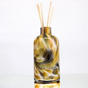 May include: A decorative glass diffuser bottle with a swirling pattern of gold, brown, and white. The bottle contains wooden reeds for fragrance diffusion. The design resembles natural stone, adding a touch of elegance to any space.