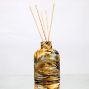 May include: A decorative glass diffuser bottle with a swirling pattern of yellow, brown, and black. The bottle contains wooden reeds for fragrance diffusion. The bottle is approximately 15 cm tall.