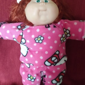 May include: A Cabbage Patch Kid doll with red hair wearing pink pajamas with white polka dots and a Hello Kitty print.
