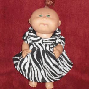 May include: A doll wearing a black and white zebra print dress. The doll has green eyes and a light pink complexion.