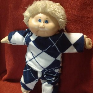 May include: A Cabbage Patch Kid doll with blonde hair wearing a blue and white checkered pajama set.