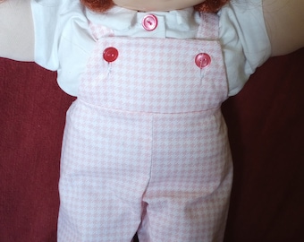 Puede incluir: Una muñeca Cabbage Patch Kid con pelo rojo que lleva una camisa blanca y un mono de pana rosa y blanco.