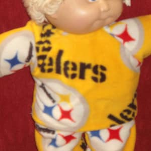 May include: A yellow and white baby doll outfit with a black "Steelers" logo and a black and white star pattern.