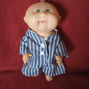 May include: A Cabbage Patch Kid doll with a red mohawk wearing a blue and white striped pyjama set.