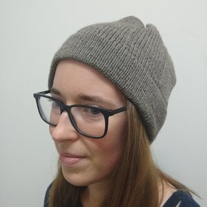 May include: A person wearing a gray knitted beanie hat with black framed glasses.