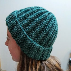 Könnte beinhalten: Eine dunkelgrüne Strickmütze mit umgeklapptem Rand. Die Mütze ist mit einem strukturierten Stichmuster gearbeitet.