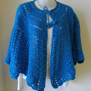 May include: A blue crocheted shawl with a tie closure. The shawl has a lacy pattern and a scalloped edge.