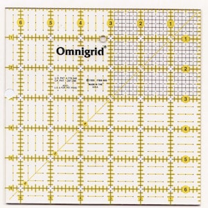 Puede incluir: Una regla Omnigrid cuadrada y transparente con líneas de cuadrícula y medidas amarillas. La regla tiene el logotipo de Omnigrid y texto que indica patentes estadounidenses y canadienses. La regla está marcada con los números 1 a 6 en los bordes.