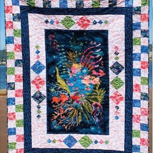 Peut inclure: Une courtepointe colorée avec une scène sous-marine. Le panneau central présente des coraux et des poissons dans des tons de bleu, d'orange et de vert. La courtepointe est encadrée d'une bordure bleu marine et d'un motif en damier rouge, bleu et vert. Le texte "Panel Bliss" est en haut.
