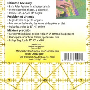 Puede incluir: Una regla de acolchado Omnigrid de 12,70 cm x 25,40 cm. La regla transparente presenta líneas de cuadrícula amarillas, marcas de ángulo y texto. El texto incluye "Ultimate Accuracy" y "Made in USA".