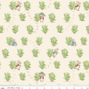 Könnte beinhalten: Ein cremefarbener Stoff mit einem sich wiederholenden Muster aus Peter Rabbit-Figuren in blauen Jacken und braunem Fell, durchsetzt mit grünen Salatköpfen und kleinen braunen Fußabdrücken. Ein 30-cm-Lineal ist am unteren Rand sichtbar.