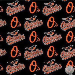 May include: Black fabric with a repeating pattern of orange and white "Orioles" logos with a bird graphic. The logo includes the letter "O" with an apostrophe and the word "Orioles".
