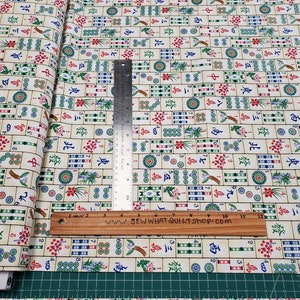 Puede incluir: Tela crema con un patr&oacute;n repetido de fichas de Mahjong coloridas. Las fichas presentan varios s&iacute;mbolos, n&uacute;meros e ilustraciones. Una regla met&aacute;lica y una regla de madera est&aacute;n colocadas sobre la tela. El texto "SEW WHAT QUILT SHOP.COM" es visible.